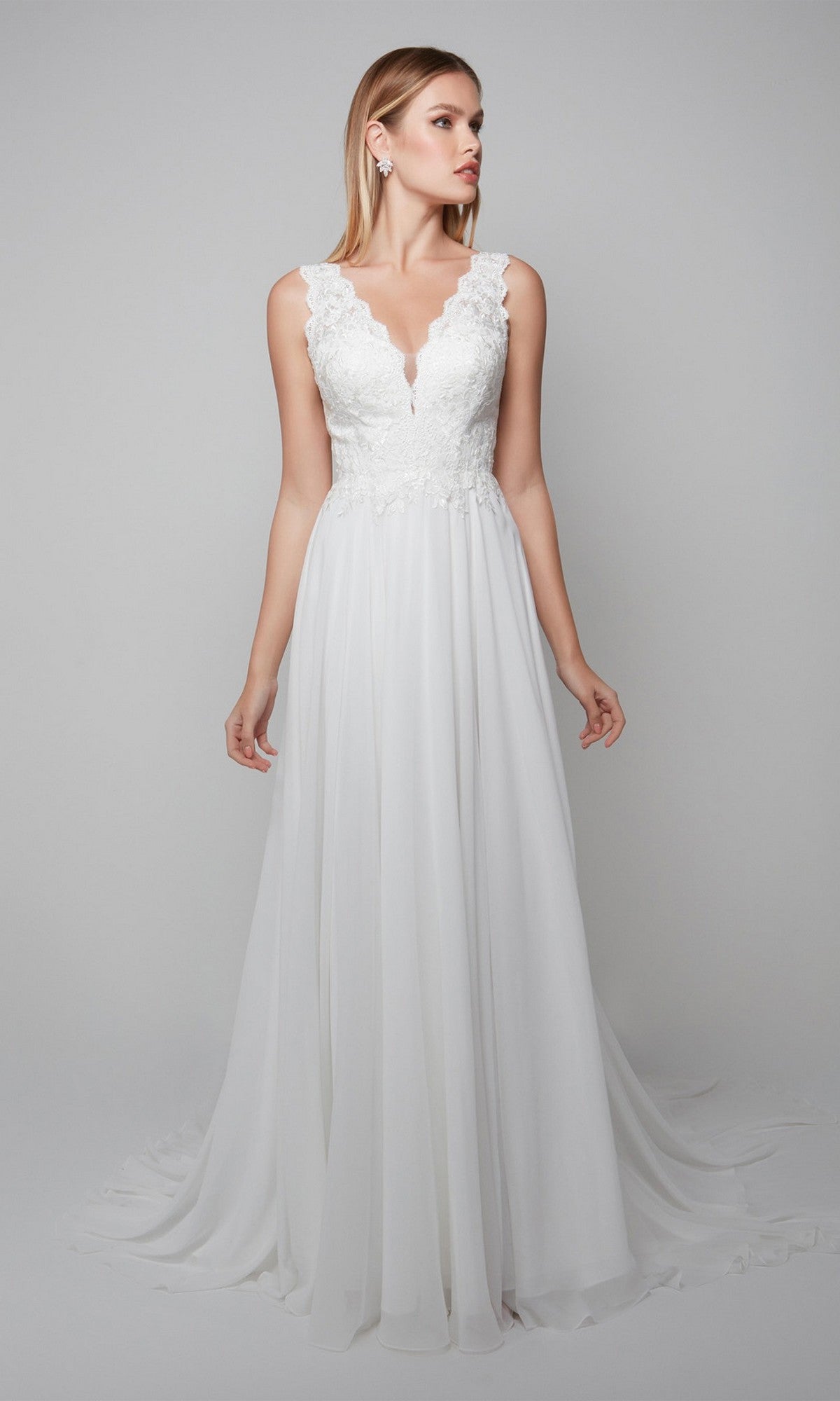 A woman stands against a plain light gray background wearing the Alyce 7071 Long White Dress—a sleeveless lace chiffon gown with a V-neckline and flowing skirt.